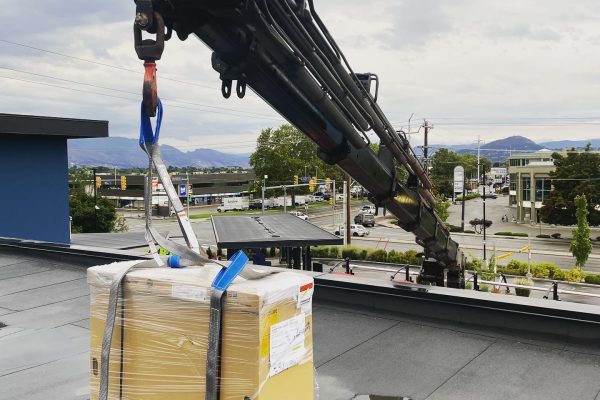 CE121736-F264-4CE6-85CF-037435F2E502 Crane lowering a packaged rooftop HVAC unit onto a commercial building